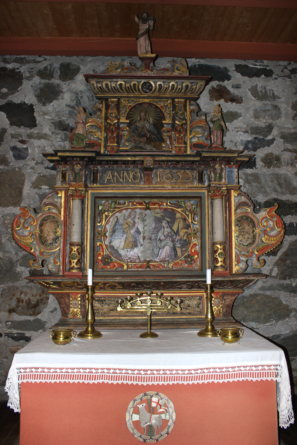 Detalj av altertavlen i Logtun kirke, utskåret i 1652 og malt i 1655, med ornamental dekorasjon og figurer, foran alterbord med lysestaker.