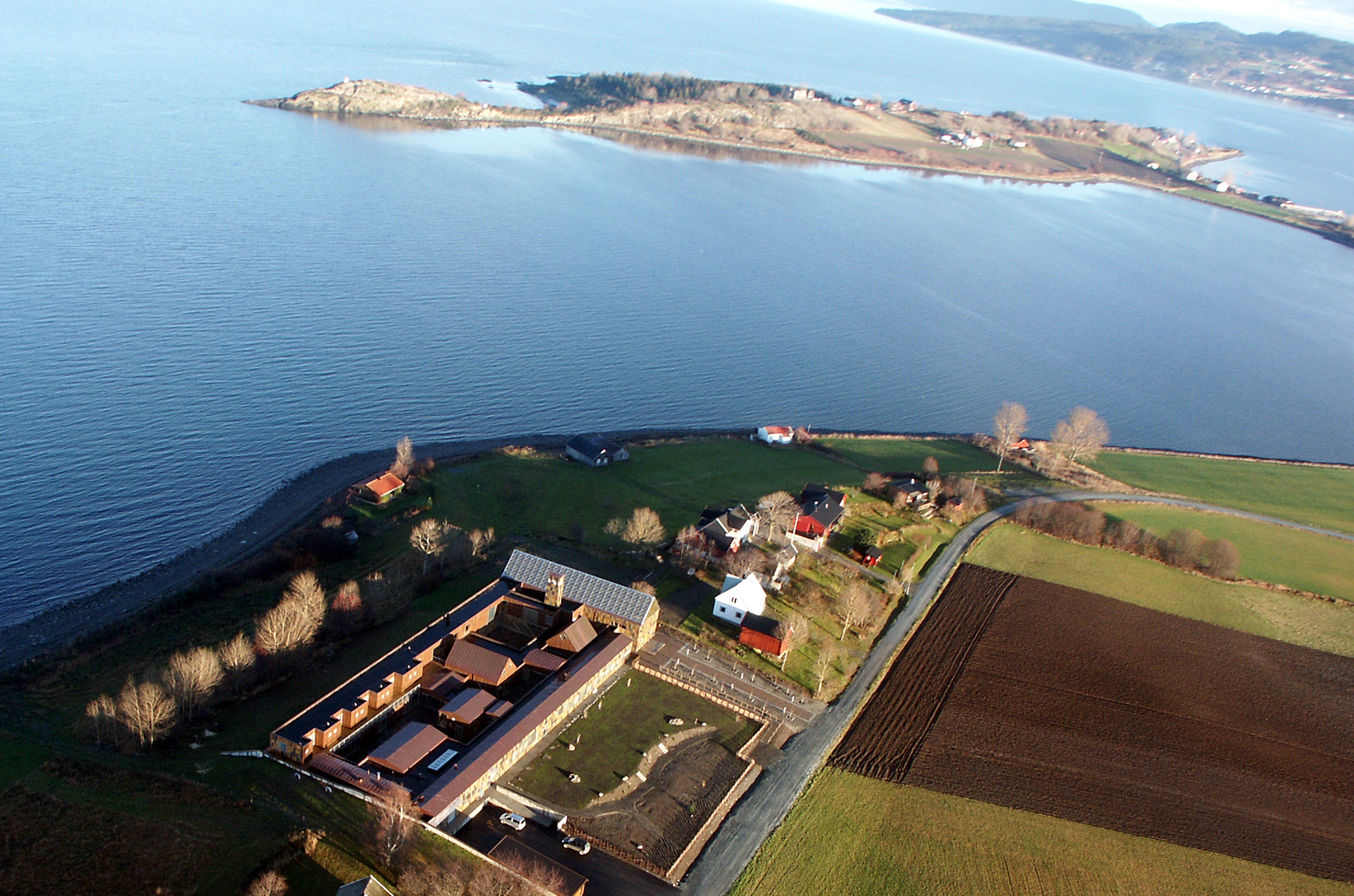 Oversiktsbilde av Tautra Mariakloster og omgivelsene, med sjøen i bakgrunnen og ulike bygninger i forkant.