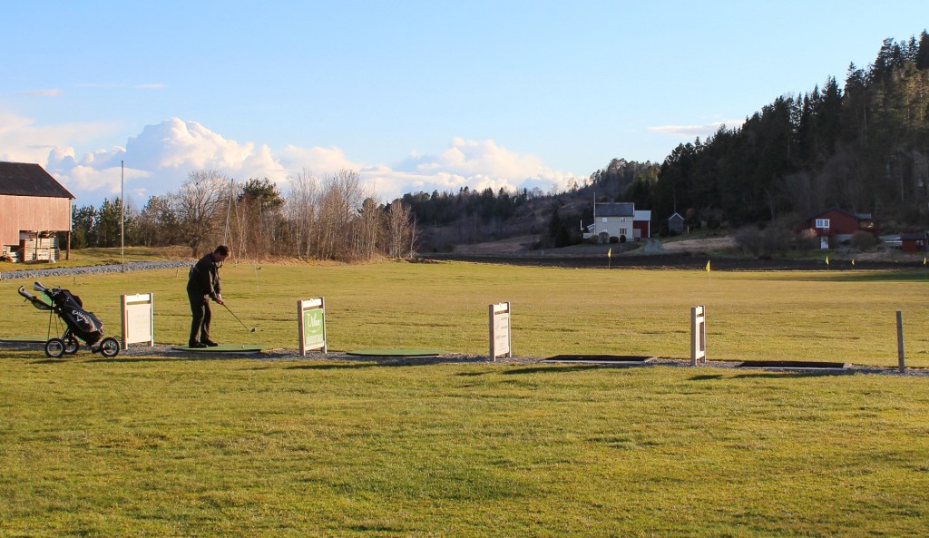 En golfer som praktiserer slag på driving range i Vågen, med en golfvogn ved siden av.