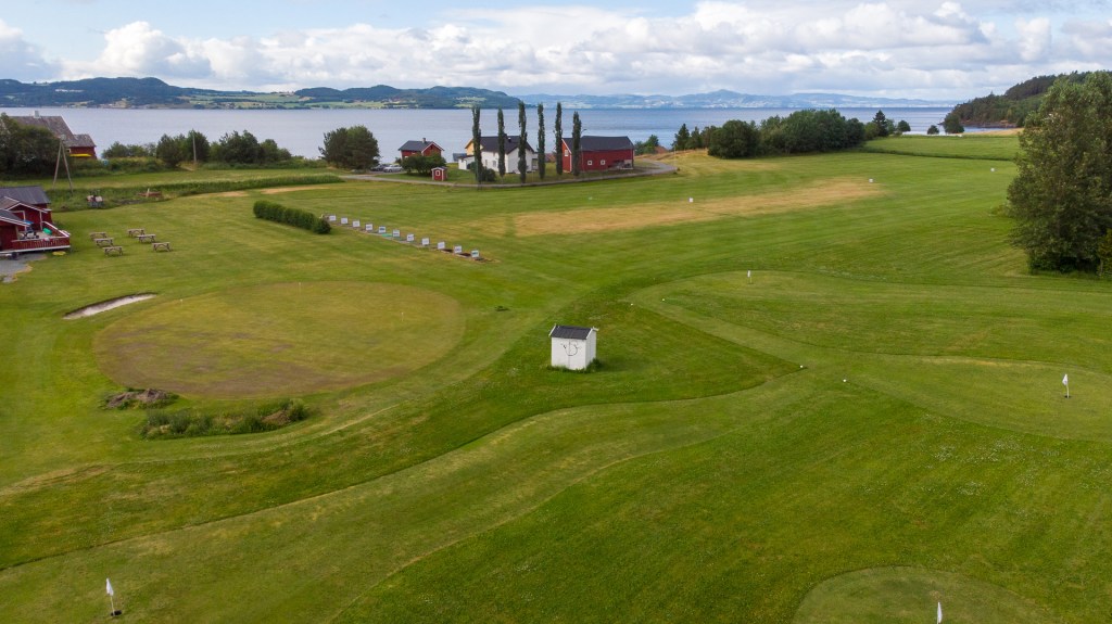 Landskapsbilde av frodig golfbane med utsikt over sjøen og omgivelser i bakgrunnen.