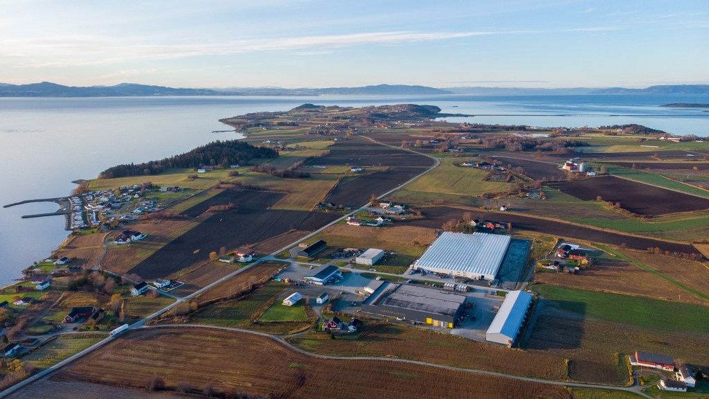 Luftbilde av Frosta med åkerlandskap, gårdsbygninger og Trondheimsfjorden i bakgrunnen.