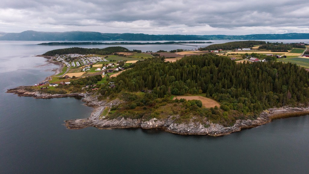 Luftbilde av Frosta med naturlandskap, gårder og campingplass langs kystlinjen.