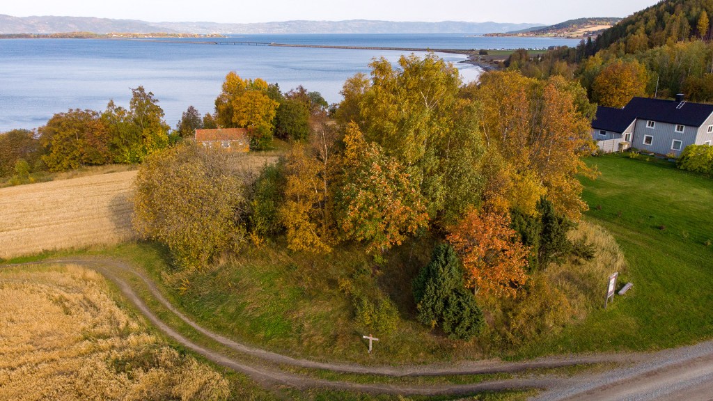 Utsikt over frodig kulturlandskap med trær i høstfarger og sjøutsikt i bakgrunnen.