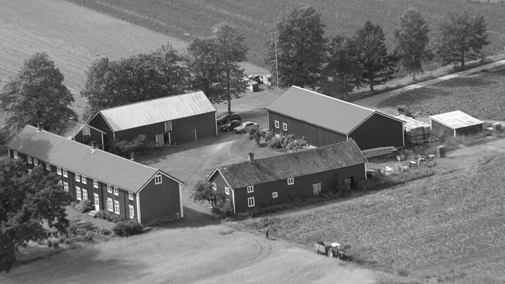 Luftbilde av en gård med flere bygninger omgitt av åker og trær, typisk for kulturlandskapet i Frostating.