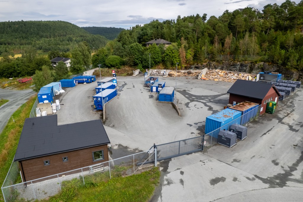 Oversiktsbilde av sorteringsanlegget på Skaret, med containere og søppeldunker for avfall, omgitt av trær og bakke i Frosta.