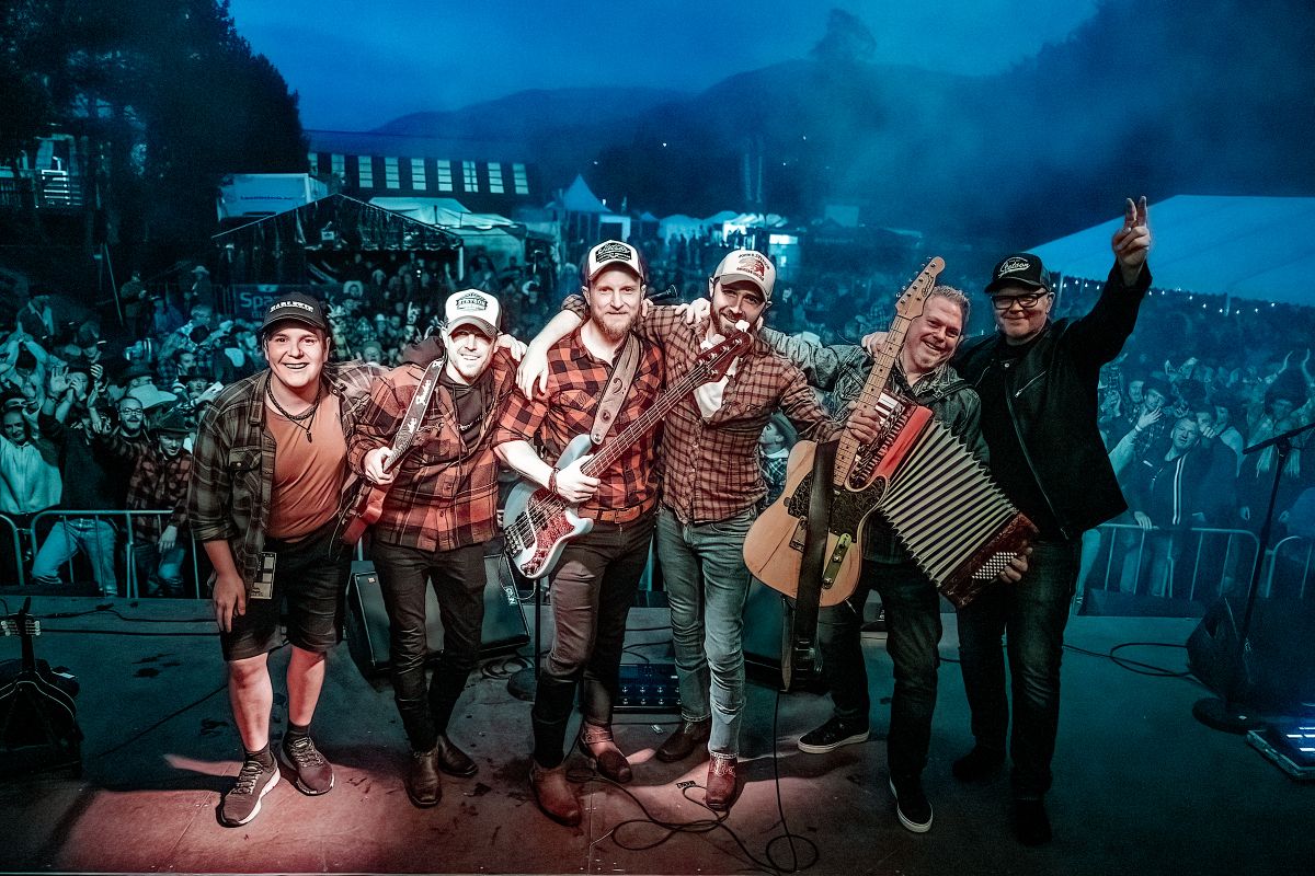 En gruppe musikere poserer på scenen foran et entusiastisk publikum under en konsert.